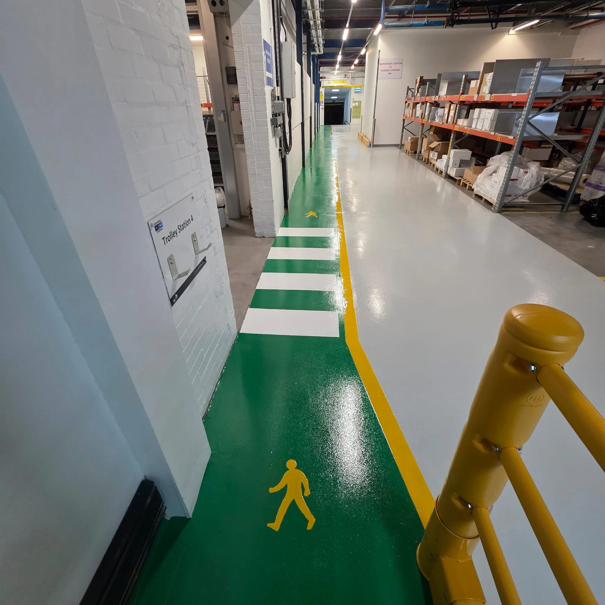 Industrial line marking with white crossing bars, green pedestrian walkway and yellow boundary line