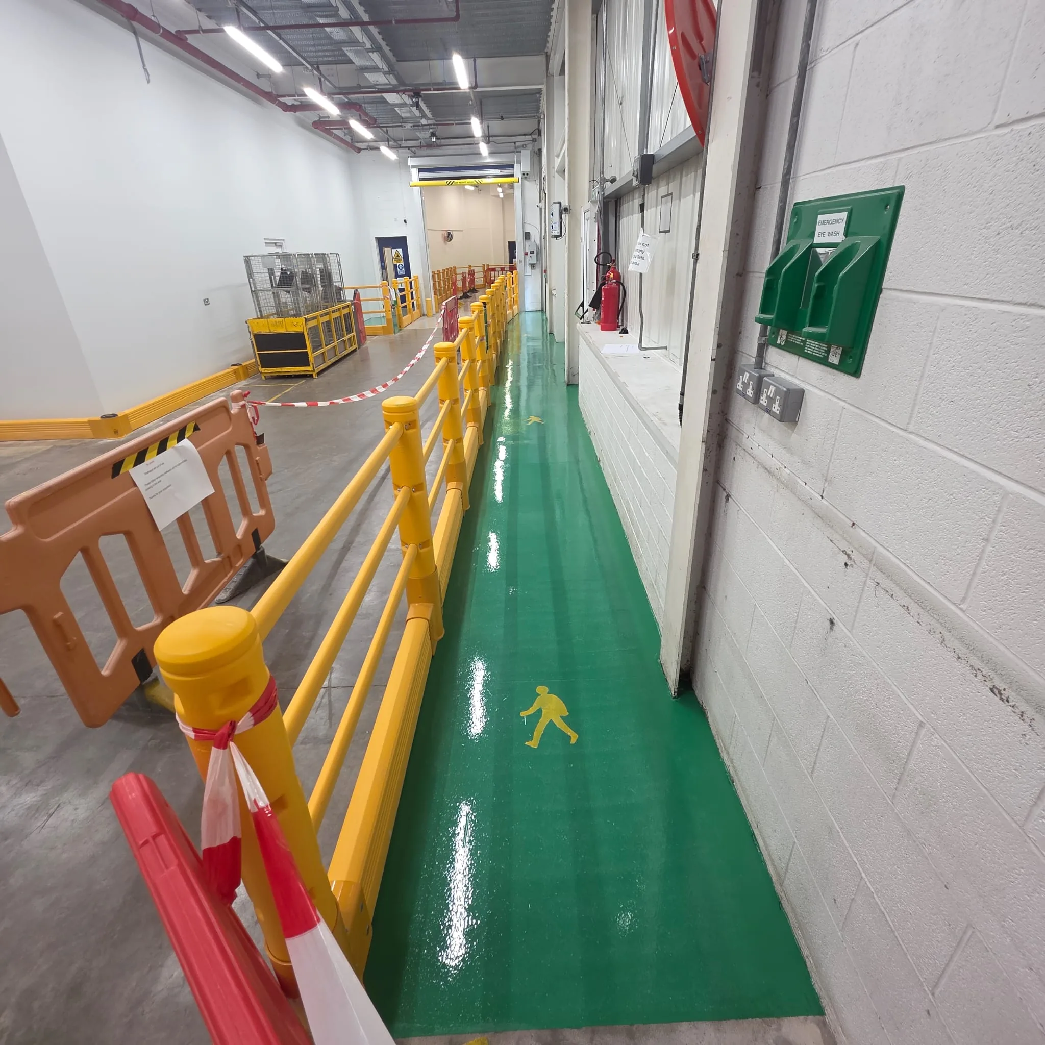 Industrial pedestrian route marked in green with yellow walking symbols beside factory barriers