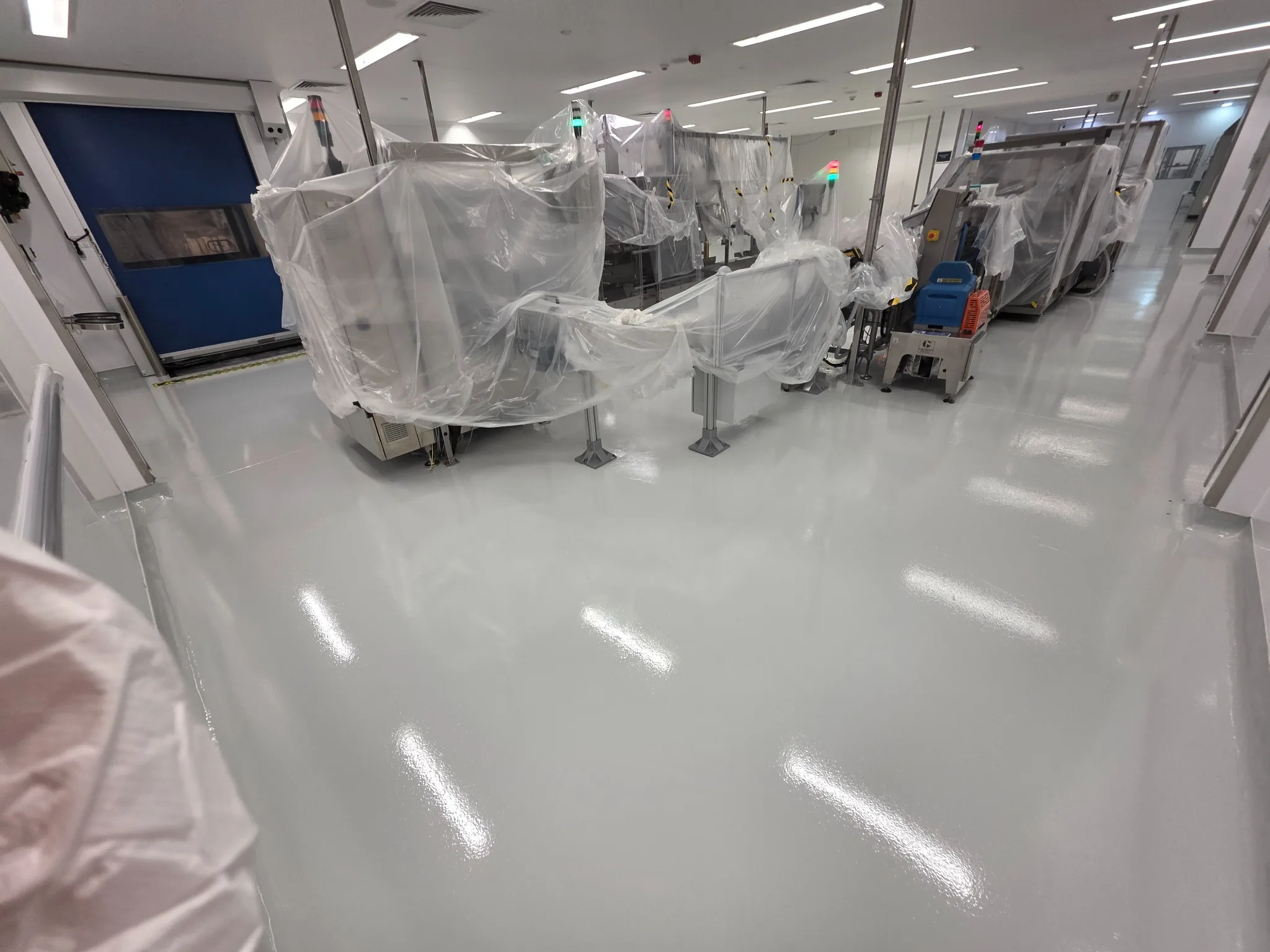 High-build epoxy flooring installed around protected pharmaceutical production machinery during a staged refurbishment